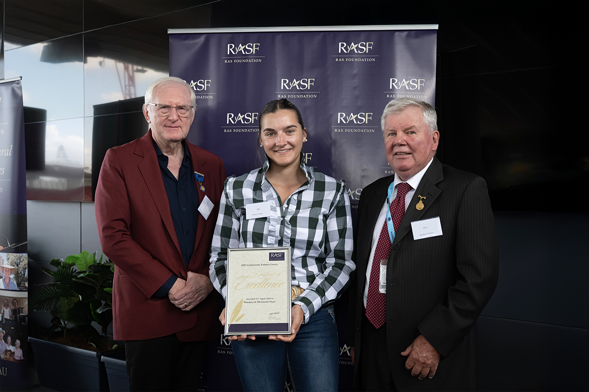 2025 RAS Community Grant recipient Lilian Lawler holding a framed certificate, standing with Dennis Wilson and Michael Millner.