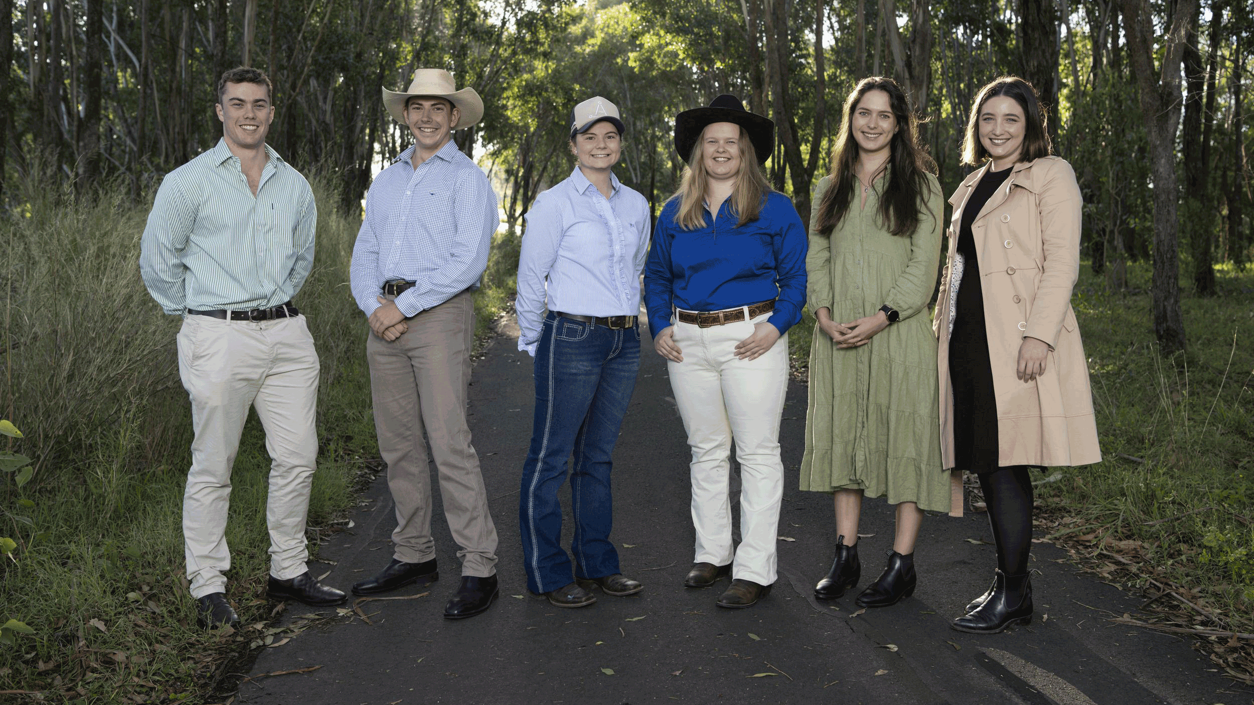 Six young finalists of the RAS Foundation Rural Scholarhip standing outside on a tree-lined path, smiling and dressed in smart rural attire.