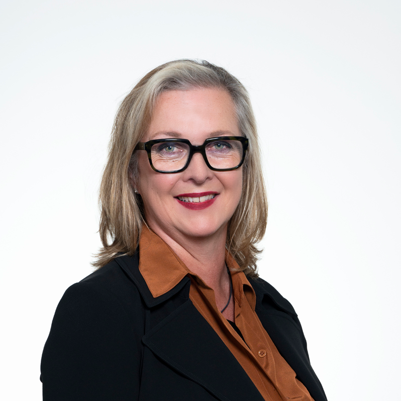 Headshot of Vice President and Board Member Alison Renwick, smiling and wearing glasses and a black jacket over a brown shirt.