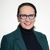 Headshot of Dairy Produce Chair and Board Member Heidi Badgery, smiling and wearing glasses and a dark green jacket over a black top.