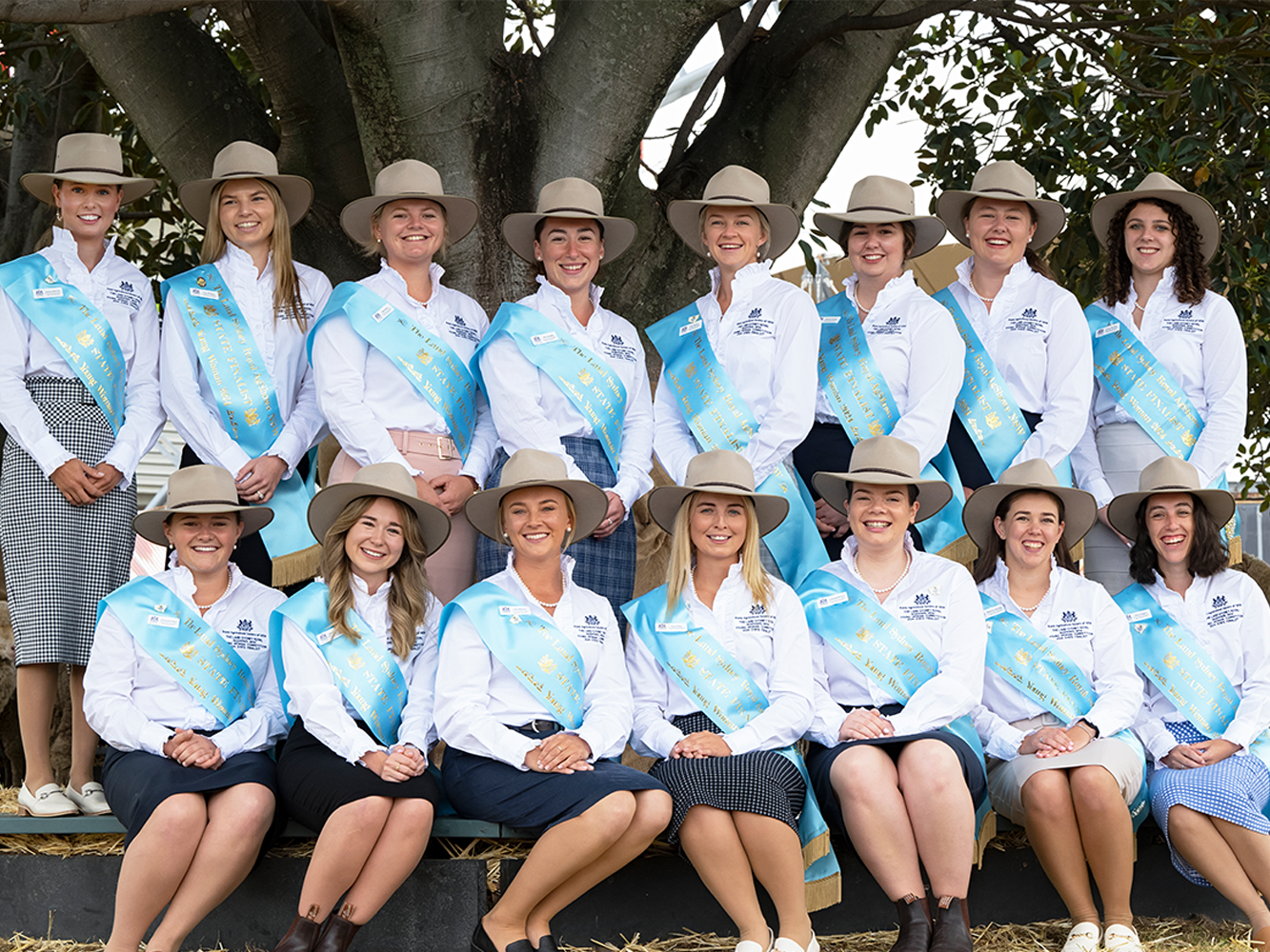 Sydney Royal AgShow NSW Young Woman finalists in white shirts, blue sashes, and wide-brimmed hats pose outdoors under a large tree.