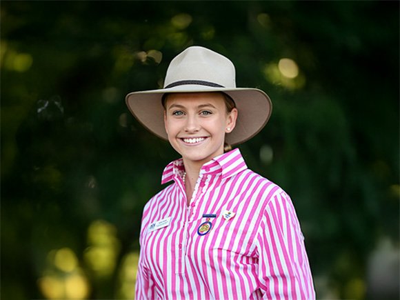 Headshot of 2025 finalist Isabel Smith, a blonde woman smiling and wearing pearl earrings with a wide-brimmed hat.