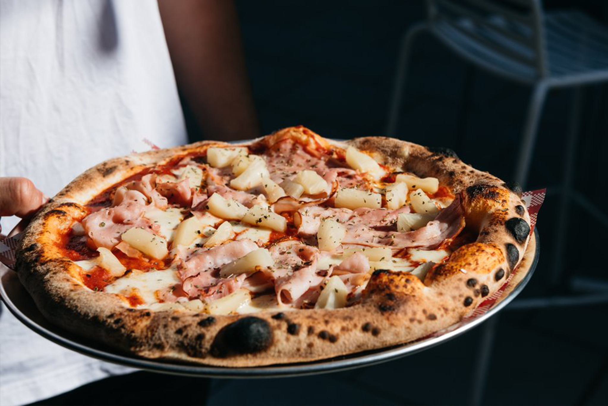 Woodfire pizza topped with ham, pineapple, and cheese, served on a silver plate at Grape, Grain and Graze Festival.