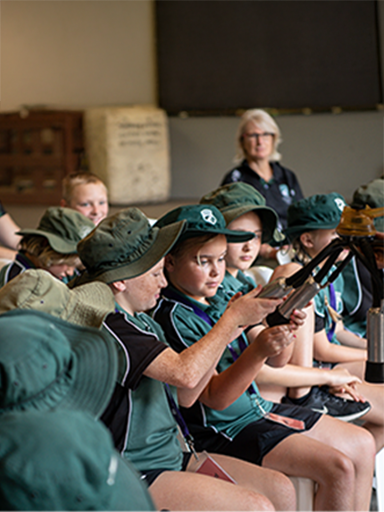 Primary school students in green uniforms and hats examining farm equipment during a Farm Day Excursion.